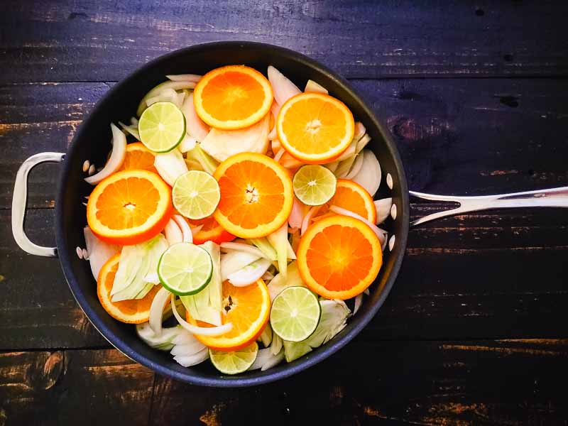 Sliced oranges, lime, fennel, and onion in a saute pan
