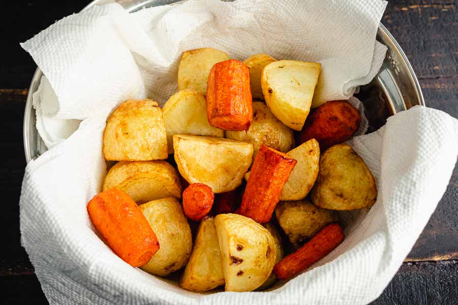 Fried potatoes and carrots draining in a paper towel-lined mixing bowl