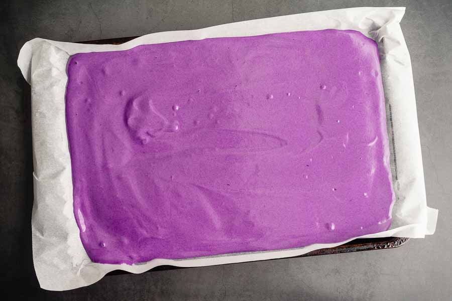 The ube cake batter poured onto a prepared sheet pan