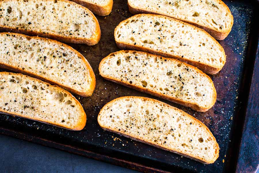 Sliced, seasoned, and toasted ciabatta bread on a sheet pan