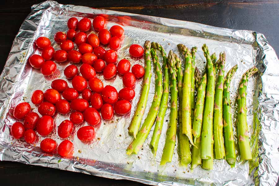 The prepped grape tomatoes and asparagus on a foil-lined sheet pan