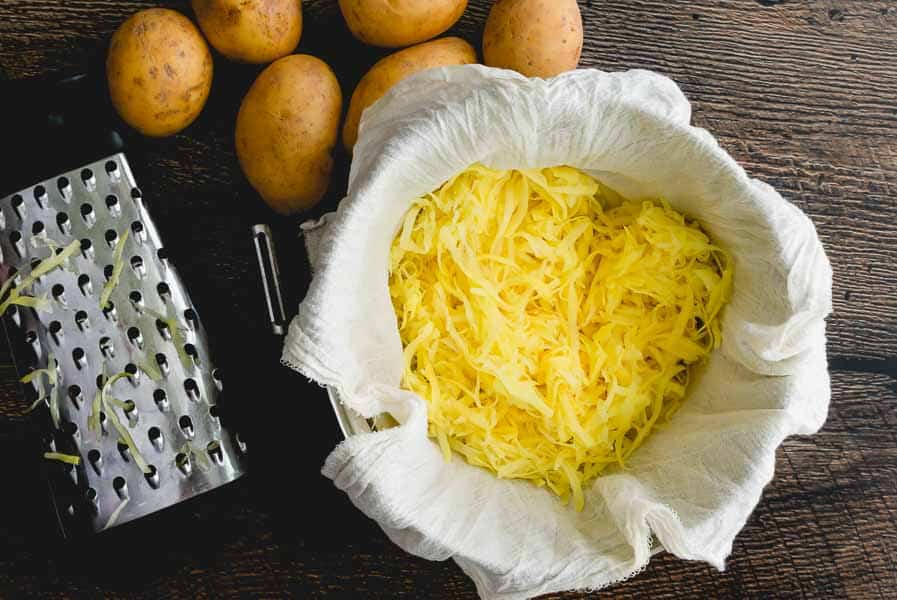 Shredded potatoes in a cheese cloth-lined mixing bowl