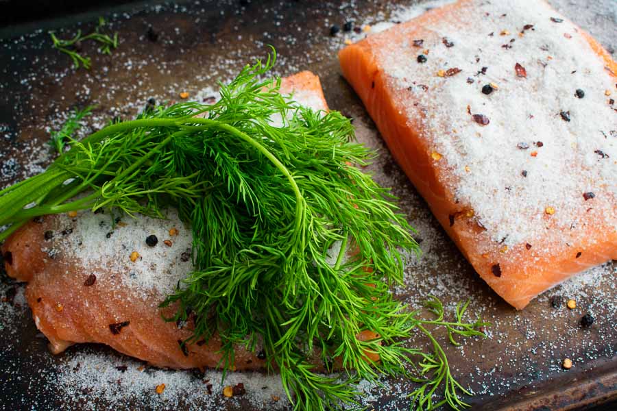 Two halves of the salmon fillet topped with salt, spices, and dill