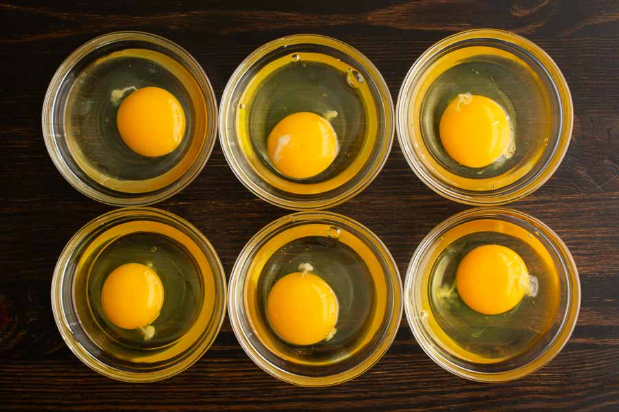Six cracked eggs in small glass bowls