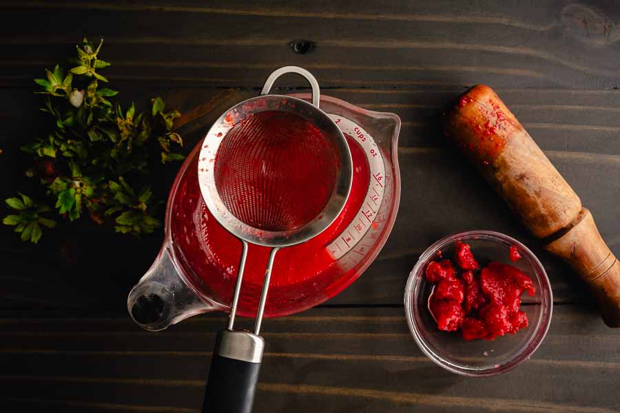 Straining pureed strawberries with a fine mesh sieve