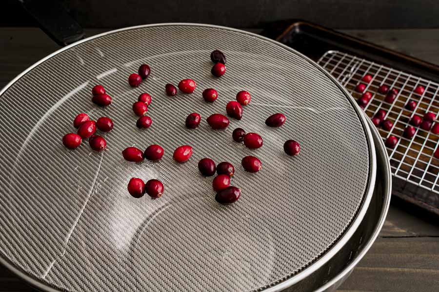 Cranberries drying on a spatter screen on over a mixing bowl